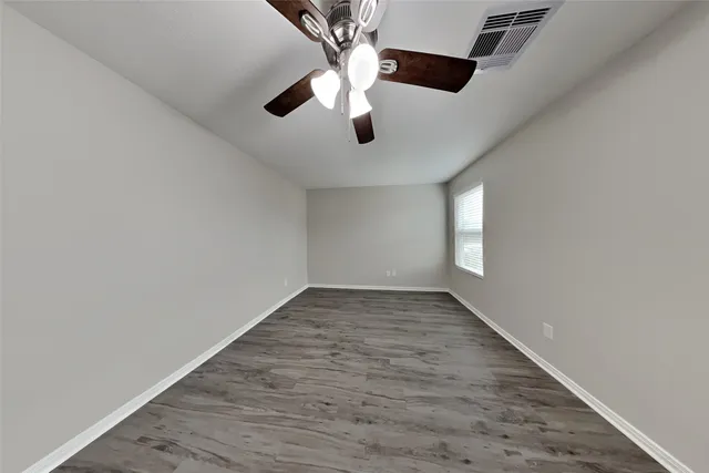 an empty room with wooden floor chandelier fan and windows