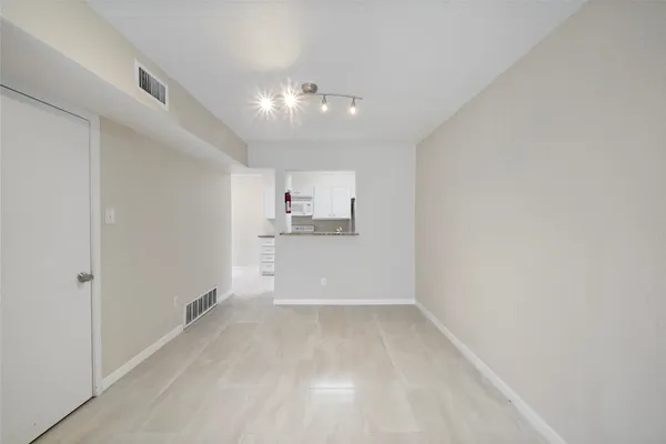 an empty room with kitchen view and wooden floor