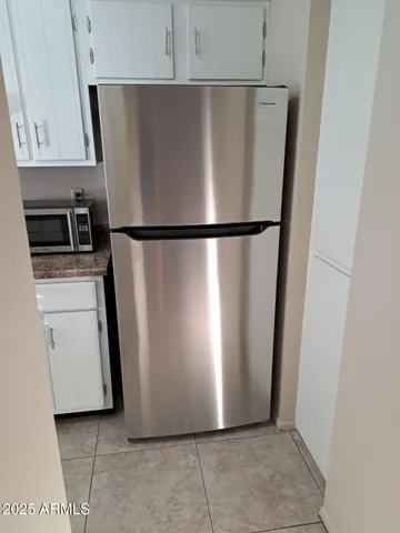 a view of a refrigerator in kitchen and an empty room with wooden floor