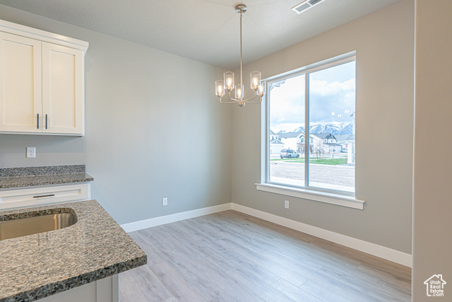 2242 South 1120 West, Unit 69 Logan, UT 84321 - Photo 8 of 26 Kitchen featuring light wood-style floors, light stone counters, hanging light fixtures, a chandelier, and white cabinetry