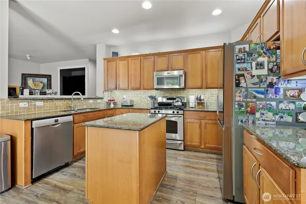 a kitchen with stainless steel appliances granite countertop wooden floor a refrigerator a stove and a dining table with wooden floor