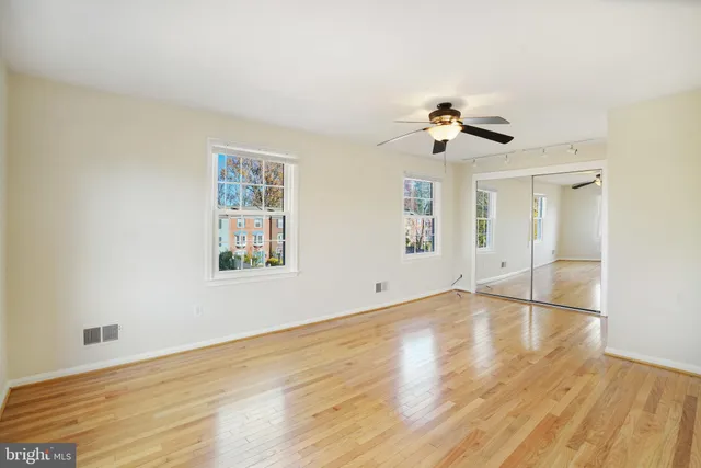 an empty room with wooden floor ceiling fan and window