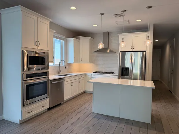 a kitchen with stainless steel appliances granite countertop a refrigerator a stove and a microwave with wooden floor