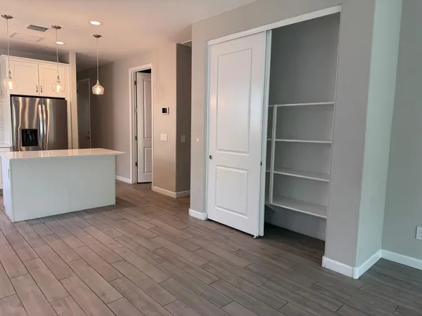 a view of an empty room with wooden floor and a kitchen