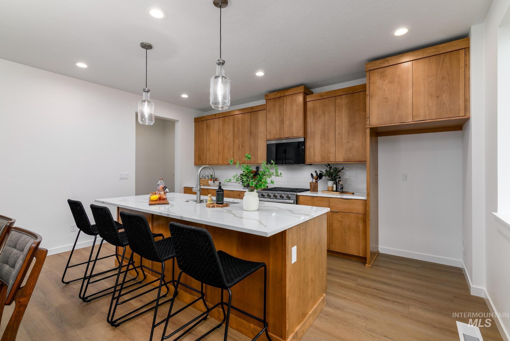 2087 West Gelding Street Middleton, ID 83644 - Photo 12 of 41 Kitchen featuring brown cabinetry, a center island with sink, pendant lighting, light stone counters, and a kitchen bar