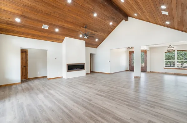 a view of an empty room with wooden floor and a kitchen