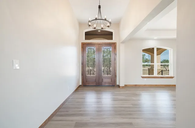 an empty room with wooden floor chandelier and windows