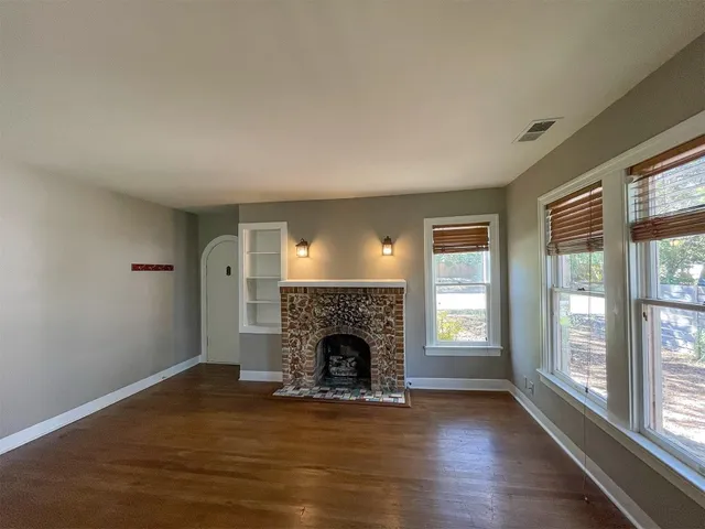 a view of an empty room with wooden floor fireplace and a window