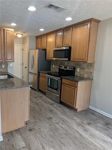 a kitchen with stainless steel appliances a refrigerator a sink a stove a microwave and wooden floor