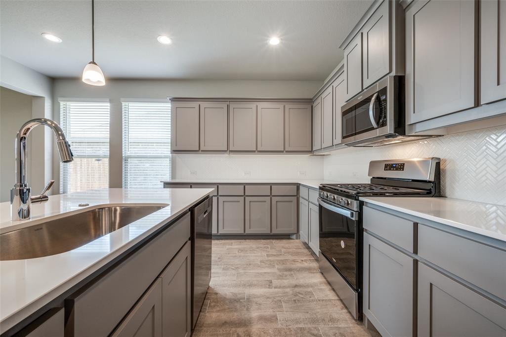 5231 Meadow Lane Krum, TX 76249 - Photo 4 of 17 Kitchen featuring an expansive island with an undermount stainless steel sink and gooseneck faucet, light-toned countertops, gray cabinetry, a stainless steel gas range with an overhead microwave, and wood-finish flooring