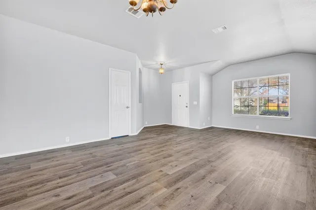 an empty room with wooden floor chandelier and windows