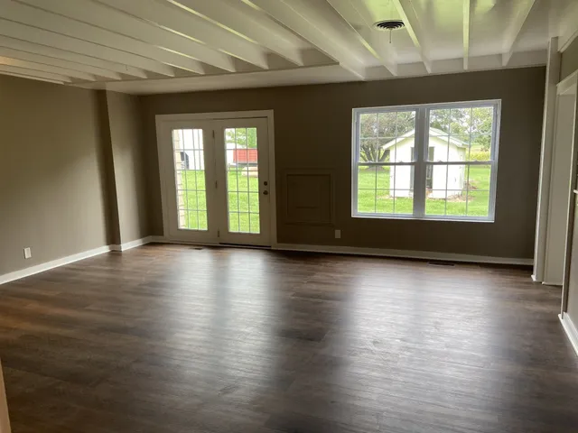 an empty room with wooden floor and windows with curtains