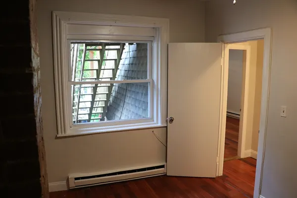 a view of an empty room with wooden floor and a window