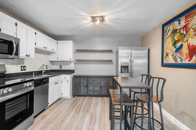 a kitchen with stainless steel appliances granite countertop a stove top oven a sink dishwasher and a dining table with wooden floor