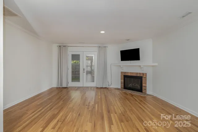 a view of an empty room with wooden floor fireplace and a window