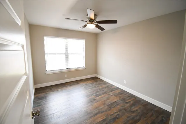 an empty room with wooden floor fan and windows