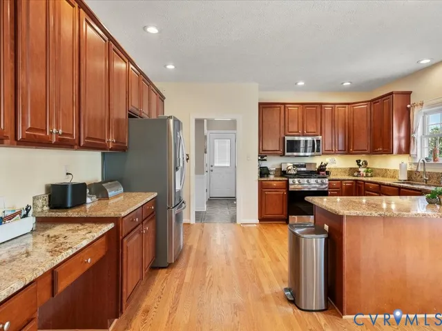 a kitchen with stainless steel appliances granite countertop a refrigerator a sink dishwasher a stove with wooden floor and cabinets