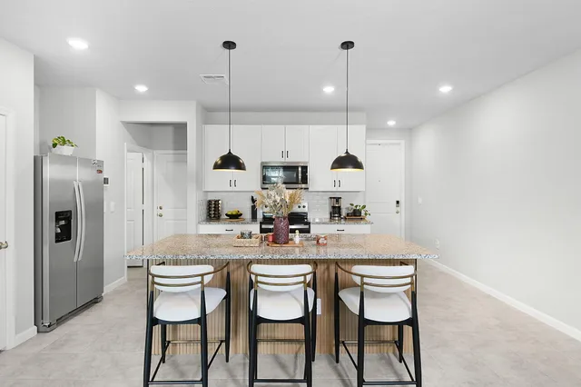 a kitchen with stainless steel appliances kitchen island granite countertop a dining table chairs and white cabinets