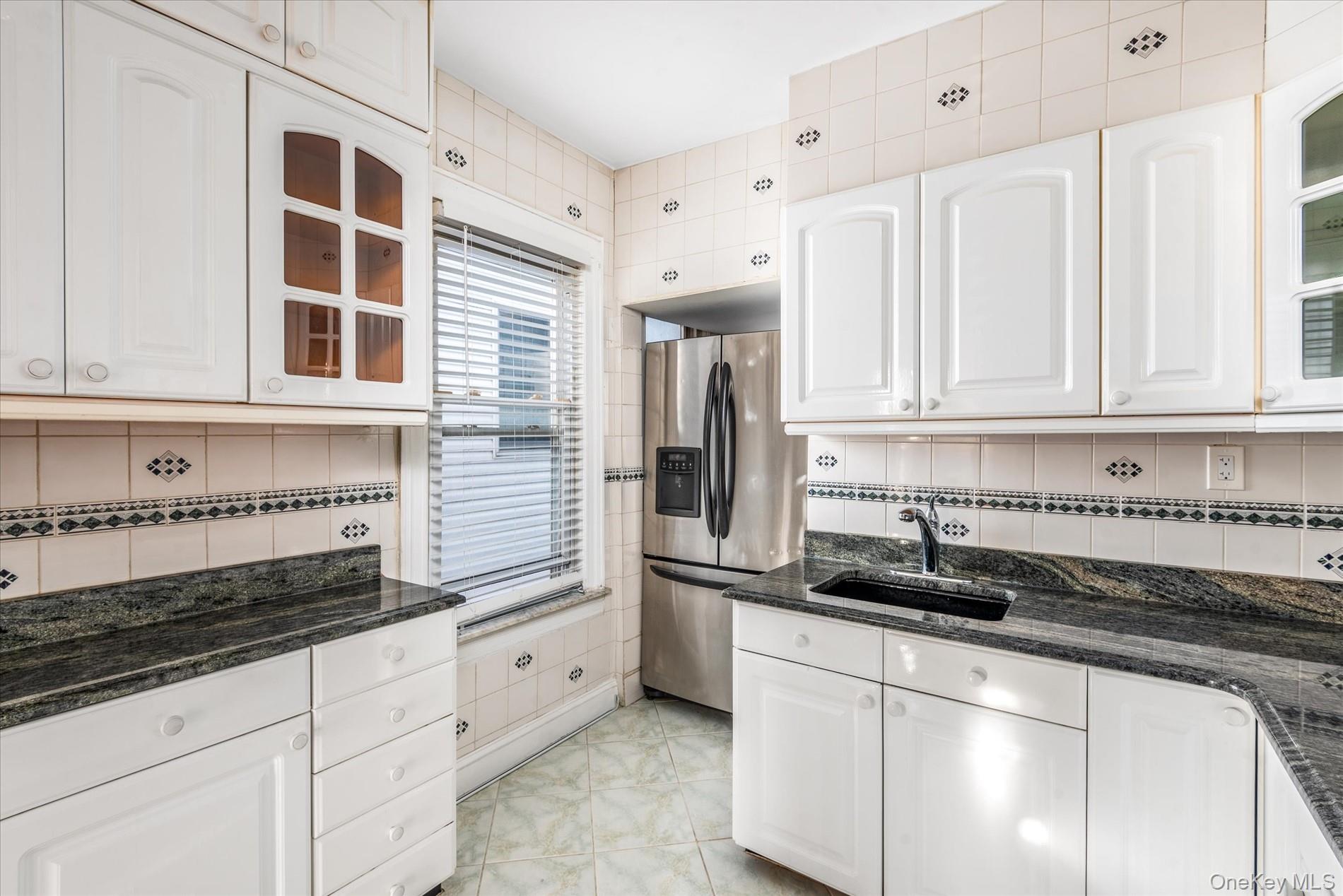93-17 123rd Street Queens, NY 11419 - Photo 15 of 40 Kitchen with glass insert cabinets, decorative backsplash, dark stone countertops, white cabinetry, and stainless steel refrigerator with ice dispenser