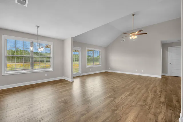 an empty room with wooden floor chandelier fan and windows