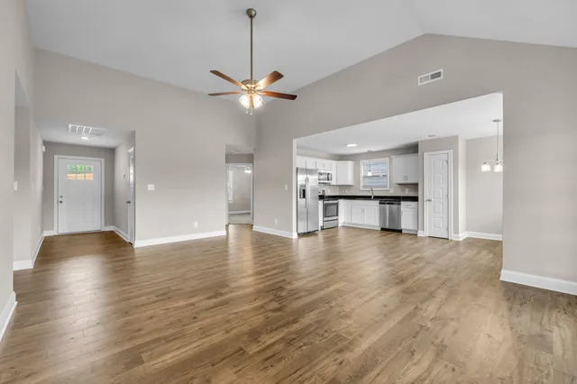 a view of empty room with wooden floor and kitchen