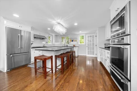 a kitchen with stainless steel appliances granite countertop a refrigerator a stove top oven a sink dishwasher and white cabinets with wooden floor