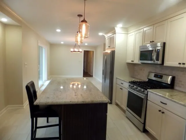 a kitchen with stainless steel appliances granite countertop a stove a refrigerator a kitchen island a sink a stove a dining table and chairs