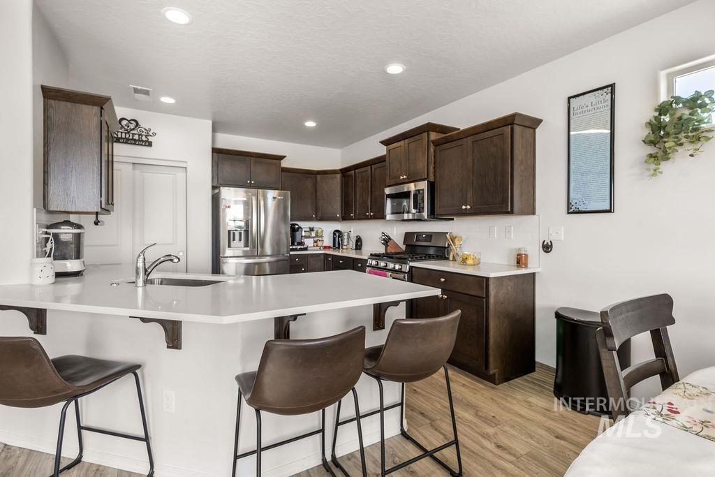 4601 Great Fls Avenue Caldwell, ID 83607 - Photo 9 of 29 Kitchen featuring a peninsula island, dark wood cabinetry, stainless steel appliances, and wood-finish flooring