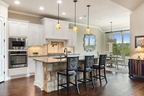 a kitchen with stainless steel appliances kitchen island granite countertop a dining table chairs and a refrigerator