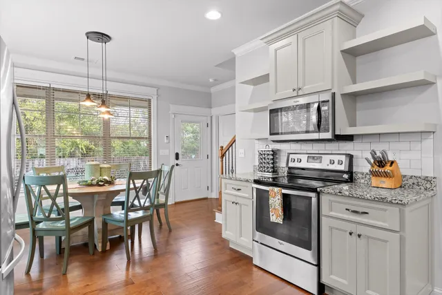 a kitchen with stainless steel appliances granite countertop a stove top oven a sink a dining table and chairs with wooden floor