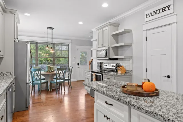 a kitchen with stainless steel appliances granite countertop a stove a refrigerator a sink a dining table and chairs with wooden floor