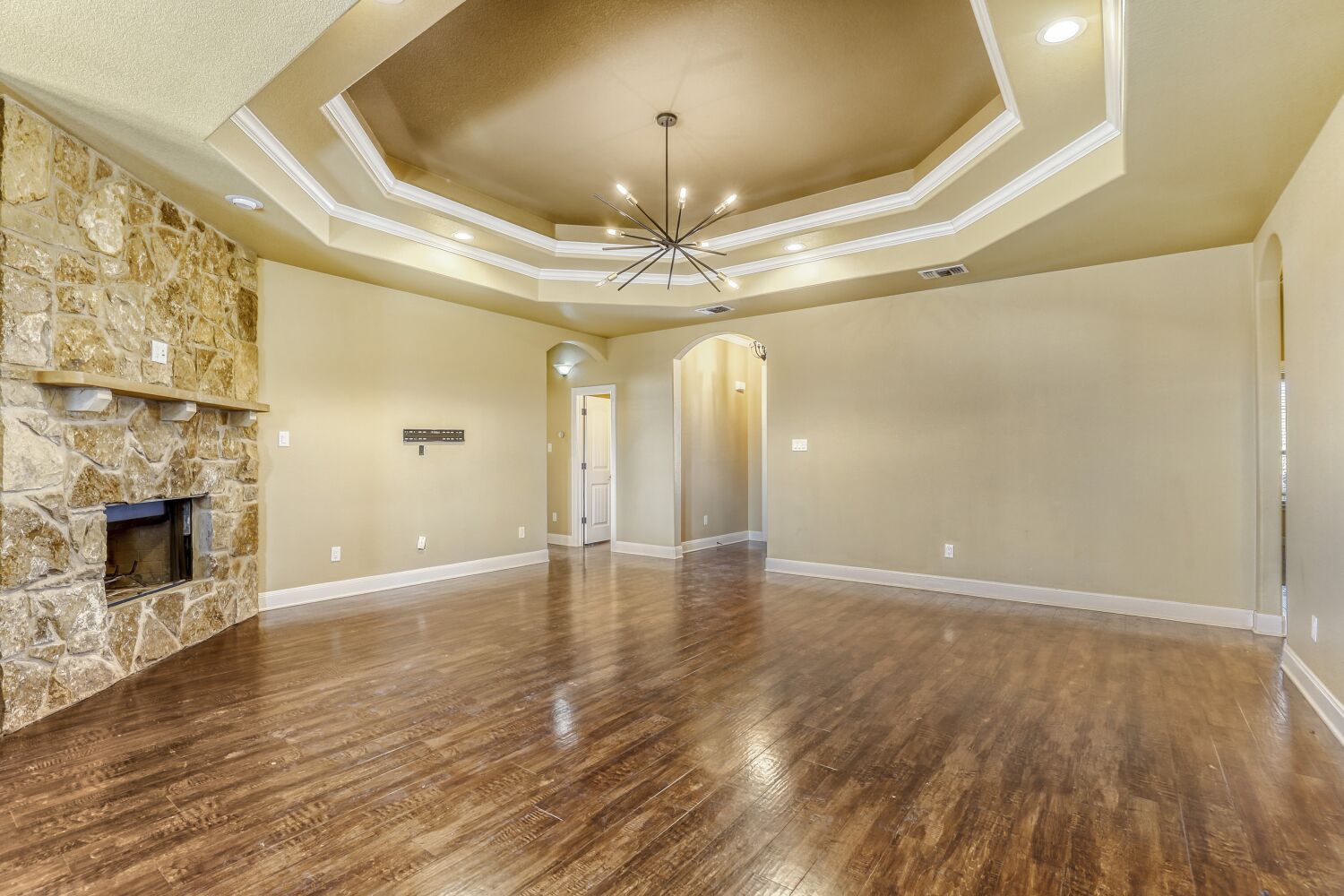 329 Jake Drive Jarrell, TX 76537 - Photo 4 of 17 Unfurnished living room featuring arched walkways, suspended lighting, a stone fireplace, crown molding, and dark wood-type flooring