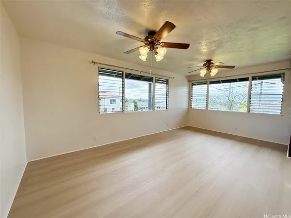 an empty room with wooden floor fan and windows