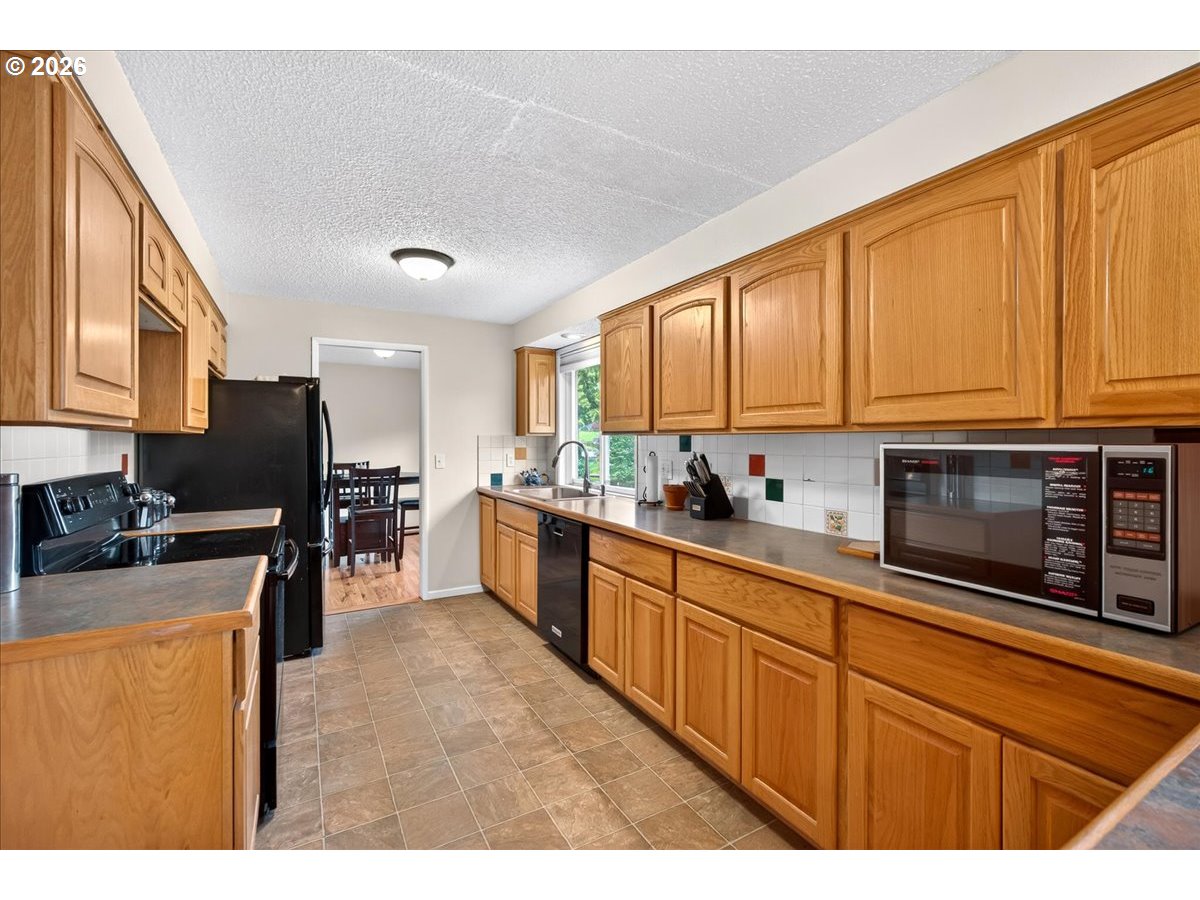 19650 Southwest Jaylee Street Beaverton, OR 97078 - Photo 23 of 46 a kitchen with stainless steel appliances granite countertop a stove top oven a sink dishwasher and a microwave oven with wooden cabinets