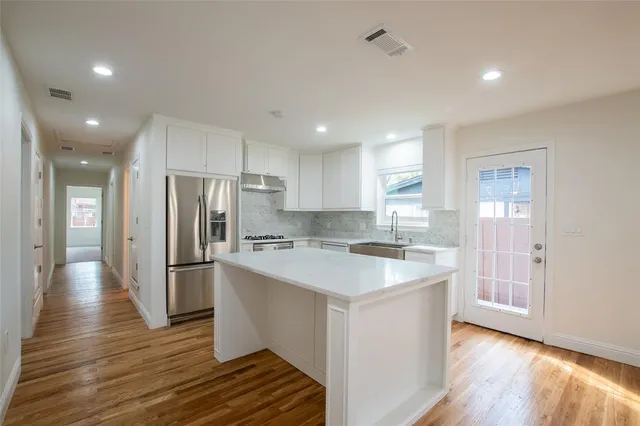 a kitchen with stainless steel appliances granite countertop a refrigerator a sink dishwasher a stove and white countertops with wooden floor