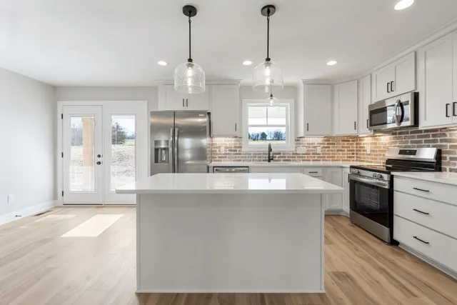 a kitchen with stainless steel appliances granite countertop a refrigerator a sink a stove and a oven with wooden floor