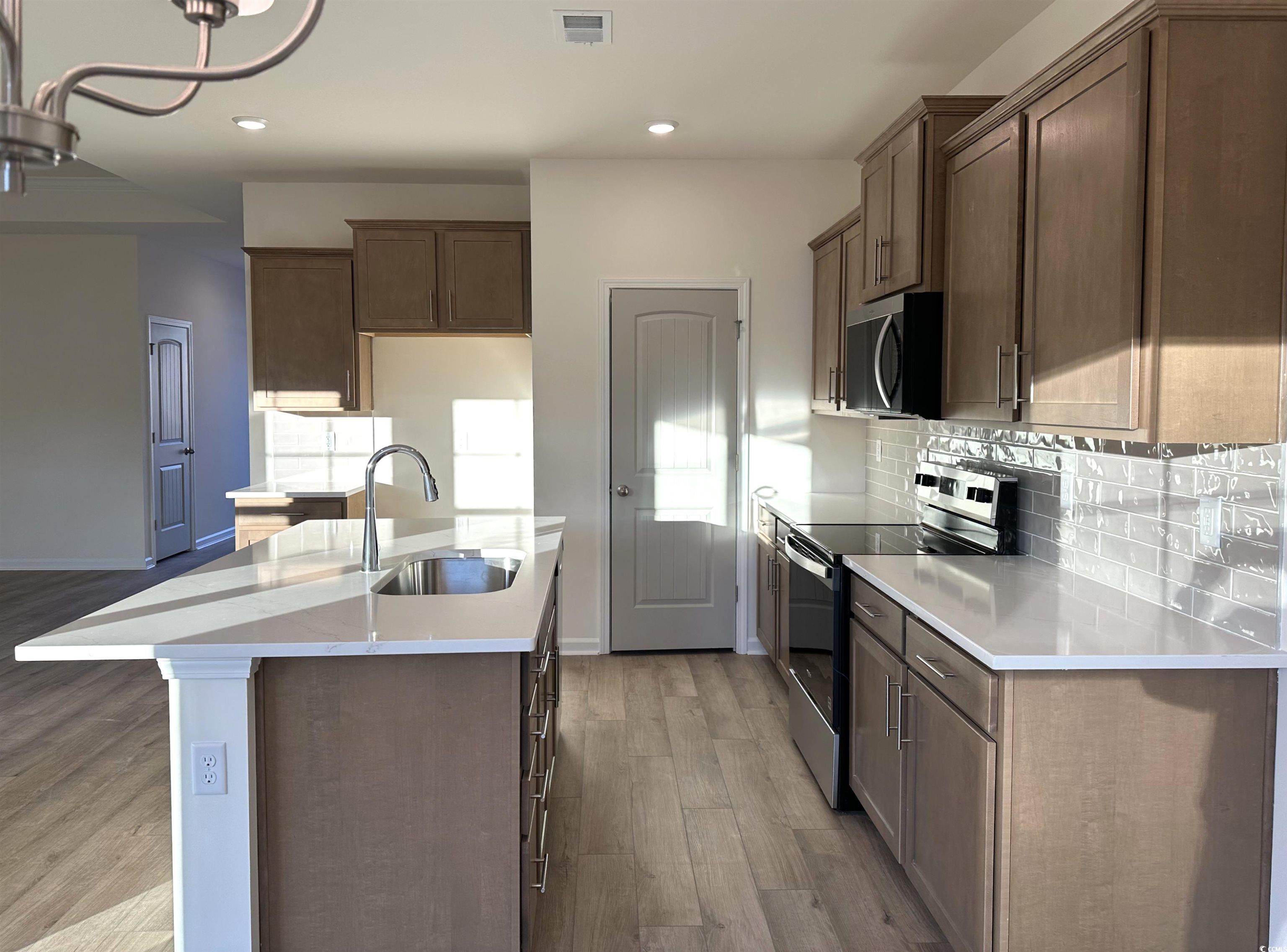 892 Birch Gdn Drive Longs, SC 29568 - Photo 3 of 15 Kitchen with stainless steel appliances, dark wood-style flooring, backsplash, light stone counters, and a kitchen island with sink