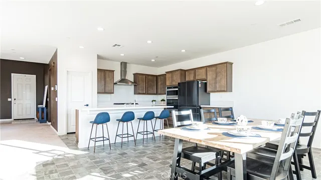 a kitchen with stainless steel appliances kitchen island granite countertop a dining table chairs and a refrigerator