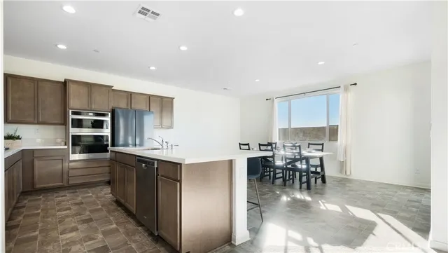 a kitchen with stainless steel appliances kitchen island granite countertop a table chairs sink and cabinets