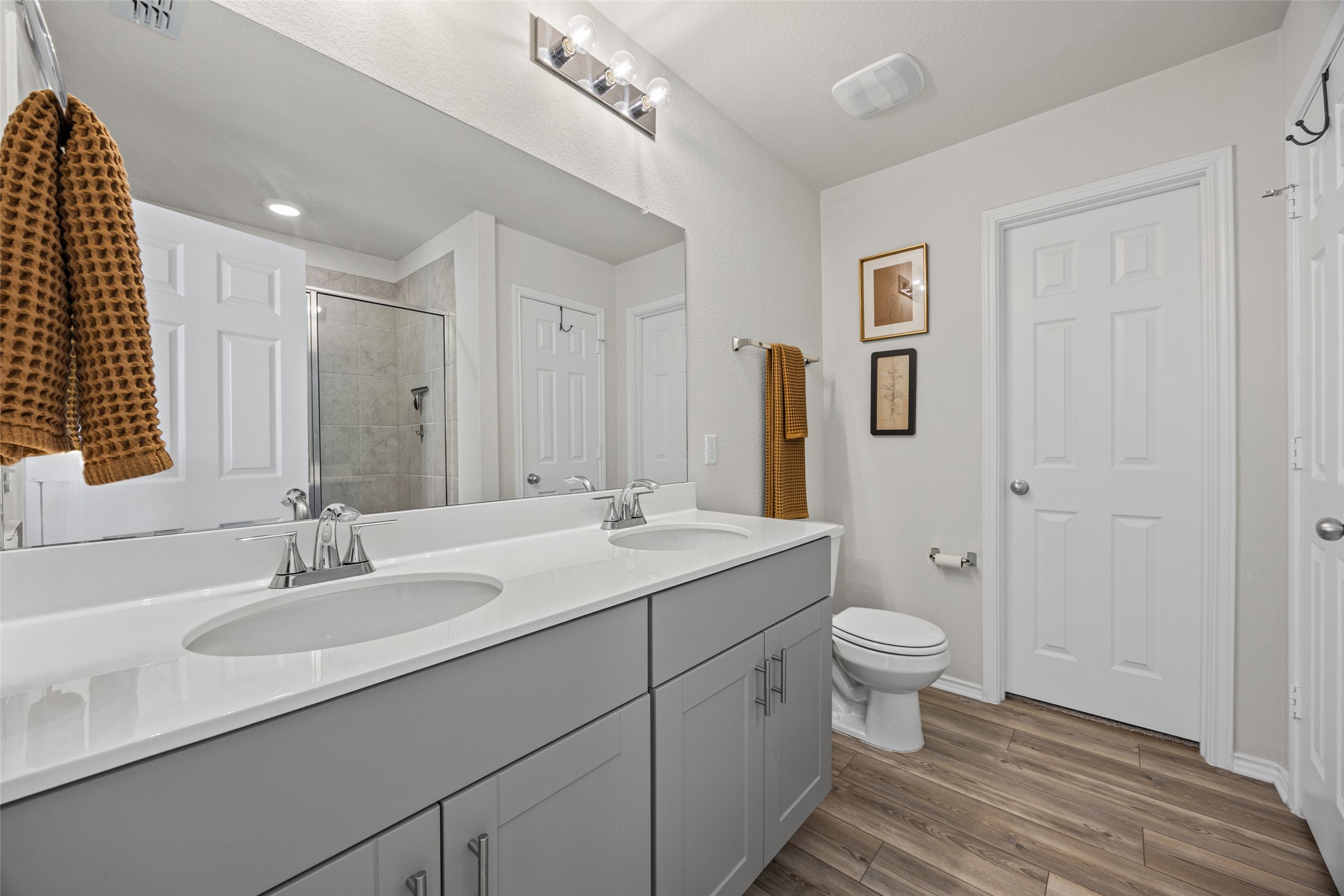 208 Orange Road Buda, TX 78610 - Photo 14 of 31 A sleek double vanity bathroom with modern gray cabinetry and natural wood-look flooring.