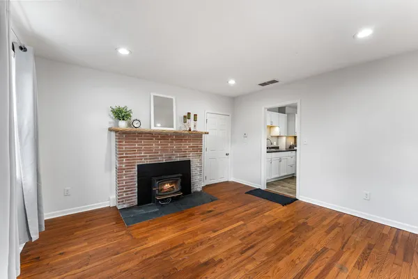 a view of an empty room with wooden floor fireplace and a window