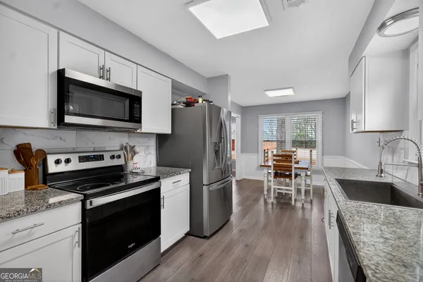 a kitchen with granite countertop a stove a sink dishwasher a refrigerator and a microwave oven with wooden floor