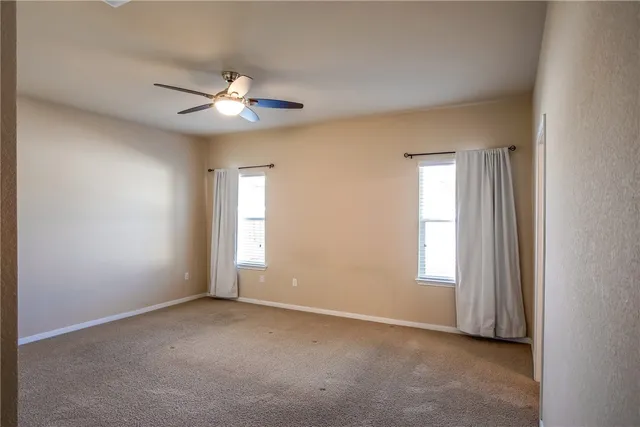 an empty room with chandelier fan and windows