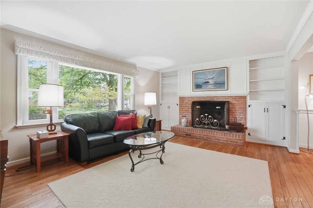 6119 Flemington Road Dayton, OH 45459 - Photo 4 of 76 This living room features a classic brick fireplace and elegant built-in shelving, complemented by rich hardwood flooring.