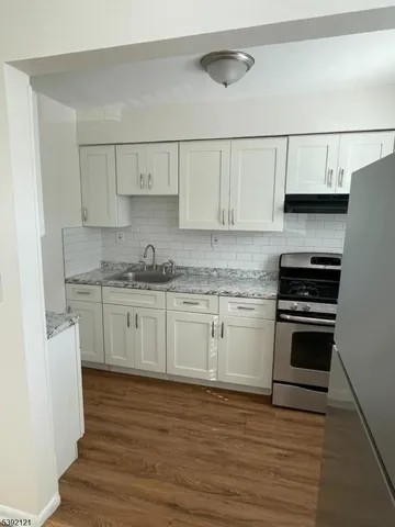 a kitchen with granite countertop a sink cabinets stainless steel appliances and wooden floor