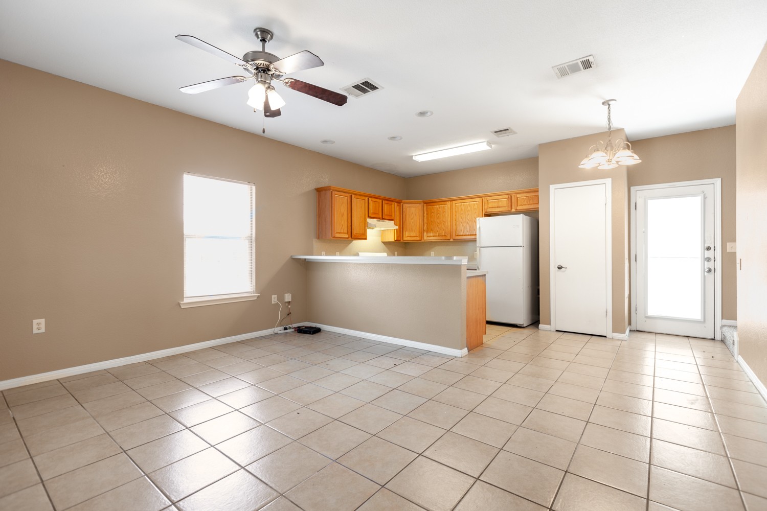 2326 Webberville Road, Unit B Austin, TX 78702 - Photo 5 of 15 Open-concept living space featuring ceramic tile flooring, a ceiling fan with light fixture, and a kitchen with wood cabinetry, a breakfast bar, and a utility door