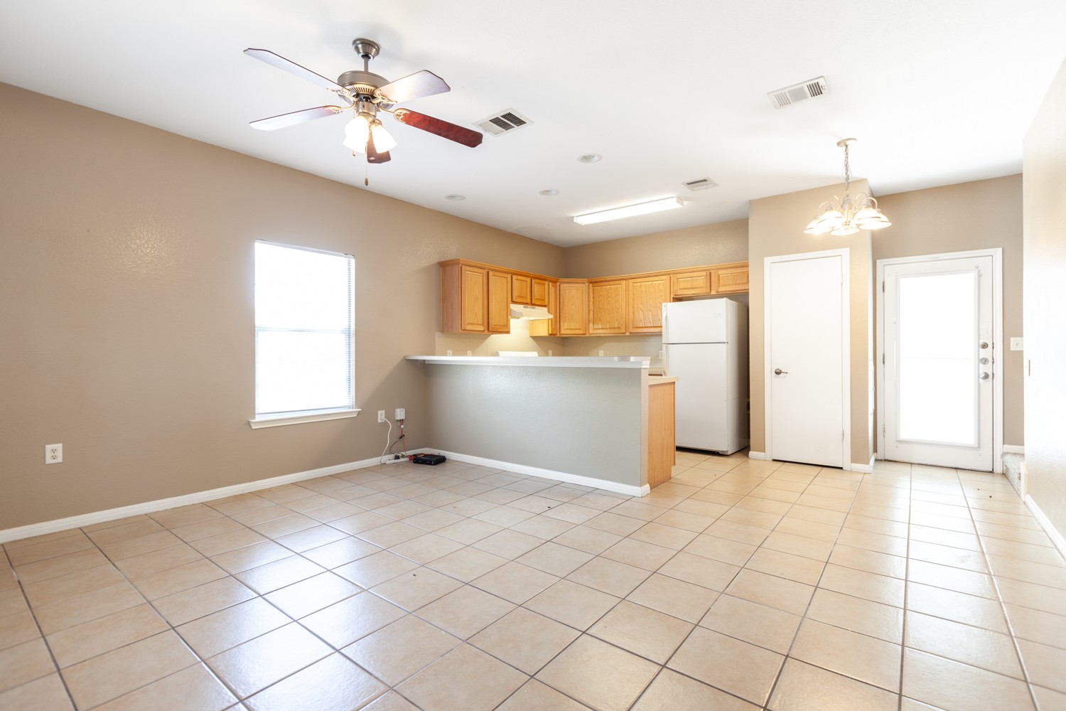 2326 Webberville Road, Unit B Austin, TX 78702 - Photo 6 of 15 Open-concept living space featuring tile flooring, a ceiling fan, and a kitchen area with wood-finish cabinetry, a breakfast bar, and a built-in refrigerator