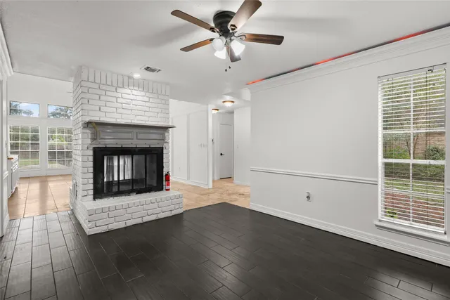 a view of a livingroom with a fireplace a ceiling fan and a kitchen view