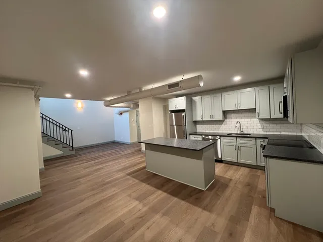 a kitchen with stainless steel appliances granite countertop a refrigerator a sink dishwasher a stove and white cabinets with wooden floor