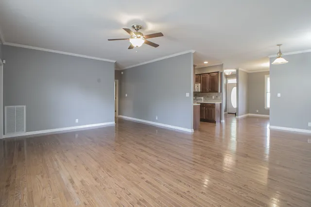 a view of an empty room with wooden floor and a ceiling fan